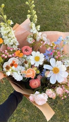 a person holding a bouquet of flowers in their hand on the grass with other flowers