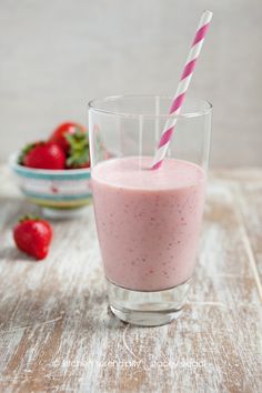 a smoothie in a glass with a pink striped straw next to it on a wooden table