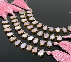 pink tasseled necklace with white and gold beads on black surface next to other jewelry items