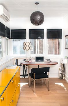 a room with a table, chair and yellow cabinet in it that has black shades on the windows