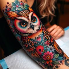 an owl tattoo on the arm with flowers and leaves around it's eyes, sitting on top of a table