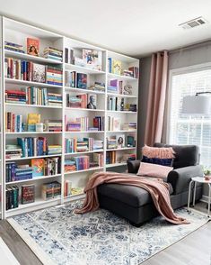 a living room filled with lots of books on top of a white book shelf next to a window