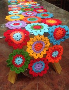 colorful crocheted flowers are lined up on a long tablecloth with wooden legs