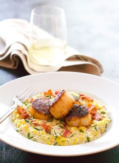 a white plate topped with scallops and grits next to a glass of wine