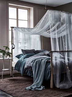 a bed with sheer curtains in a bedroom next to a table and lamp on the floor