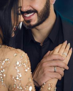 a man and woman smiling at each other with rings on their hands in front of them