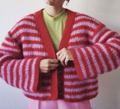 a woman wearing a red and white striped cardigan with buttons on the front, standing in front of a wall