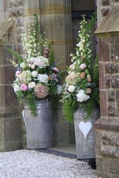 two metal buckets with flowers and greenery in front of a stone building door