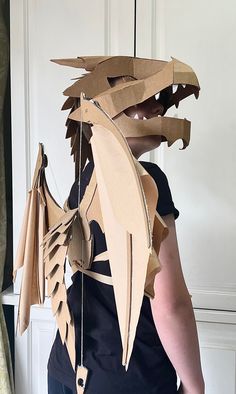 a woman is wearing a dragon costume made out of paper and cardboard strips, with wings attached to the back of her head