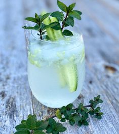 a glass filled with ice and cucumber on top of a wooden table next to leaves