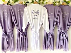 four robes hanging up against a wall with flowers in the background and two bride's names on them