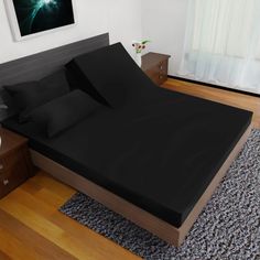 a bed with black sheets and pillows in a room next to a painting on the wall