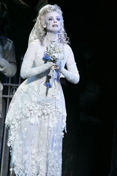 a woman dressed in white holding flowers on stage