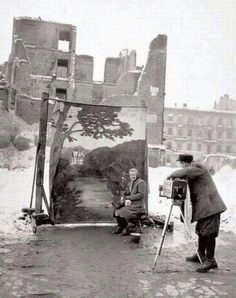 an old black and white photo of two men painting in the snow with buildings in the background