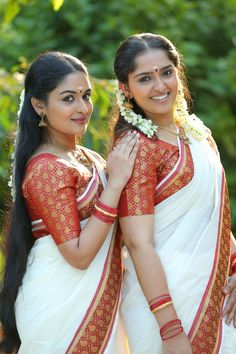 two beautiful women standing next to each other wearing white and red sari dresses with flowers in their hair