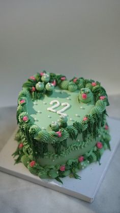 a heart shaped cake with green frosting and pink flowers on the top is sitting on a table