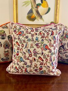 two pillows sitting on top of a wooden table next to a framed bird art piece