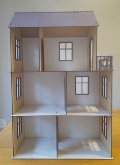 a doll house with all the windows and doors open on a wooden table in front of a white wall