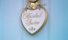 a white and gold heart shaped sign hanging on a blue door with the words bridal suite