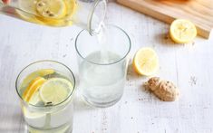 two glasses filled with water and lemons on top of a wooden cutting board next to sliced