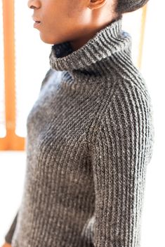 a woman wearing a gray sweater and black turtle - neck top is looking off to the side