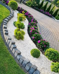 a garden with rocks and flowers on the side of it, in front of a brick walkway