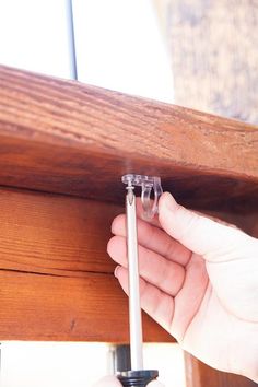 a person holding a screw in their left hand and fixing the top of a wooden table