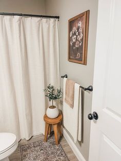 a white toilet sitting next to a wooden stool in a bathroom under a painting on the wall