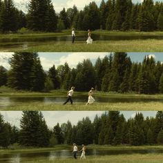 three people are running in the grass near trees