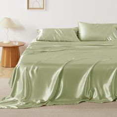 a bed with green sheets and pillows on top of it, next to a night stand