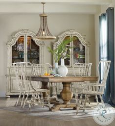 a dining room table with white chairs and a vase on top of it, in front of a china cabinet