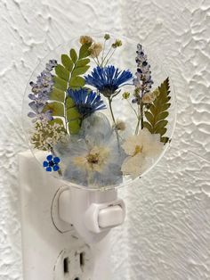 a white light switch with blue flowers and green leaves in the glass cover on it