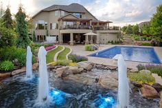 a large house with a swimming pool and waterfall in the front yard, surrounded by landscaping