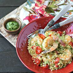 a red plate topped with rice and shrimp next to a small bowl of pesto