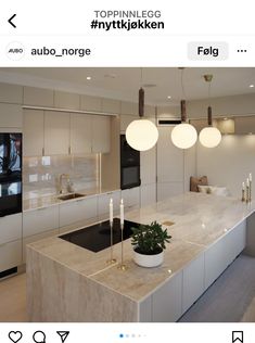 a modern kitchen with marble counter tops and white cabinetry, lights hanging from the ceiling