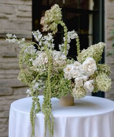 white flowers and greenery are arranged in vases on a table outside an old brick building