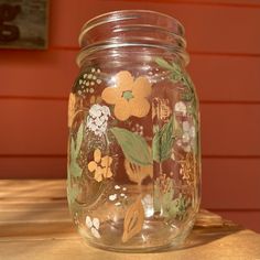 a jar with flowers painted on it sitting on a wooden table next to a red wall