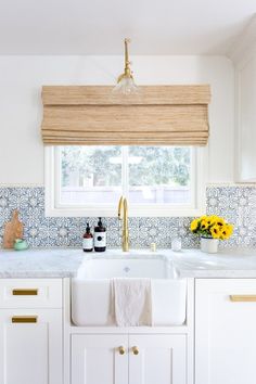 a kitchen with white cabinets and yellow flowers on the window sill above the sink