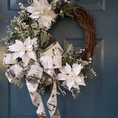 a wreath with white flowers and greenery hanging on a blue front door, decorated with ribbon