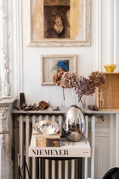 a table topped with books and vases filled with flowers next to a painting on the wall