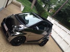 a small black car parked on the side of a brick road next to a white fence