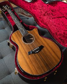 an acoustic guitar sits in its case on the floor next to a red velvet cushion