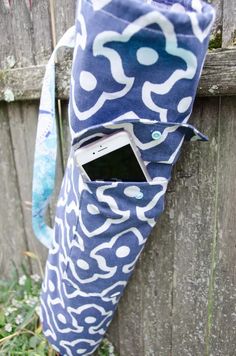 a cell phone in a blue and white bag hanging on a wooden fence next to grass