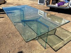 a glass table sitting on the ground in front of a truck with its doors open