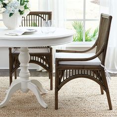 a white table and chairs in front of a large window with flowers on the windowsill