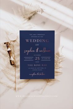 the wedding stationery is laid out on a marble surface with feathers and flowers around it