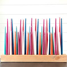 several colored candles are arranged in a wooden holder on top of a table with white planks behind them