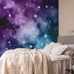 a bed sitting under a purple sky filled with stars next to a night sky wall mural