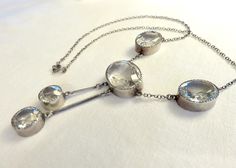 Originally $650.00. Circa 1930. Gorgeous Art Deco Era necklace featuring clear faceted crystal stones of oval and round shapes bezel set in Sterling Silver. This elegant necklace is a beautiful and versatile piece that could be worn for day or evening. It would be a wonderful piece to layer with other Deco crystal and paste pieces. Measurements: Central oval stone: Approx. 20mm x 15mm Oval stones on each side of the central Stone: Approx. 12mm x 8mm 2 round dangling round stones: Approx. 11mm in Pearl And Silver Necklace, Family Jewels, Quartz Jewelry, Elegant Necklace, Jewelry Studio, Crystal Stones, Clear Stone, Art Deco Era, Seed Pearl