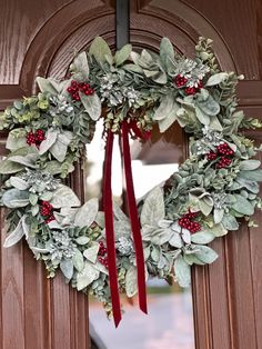 a wreath is hanging on the front door with red ribbon and greenery around it